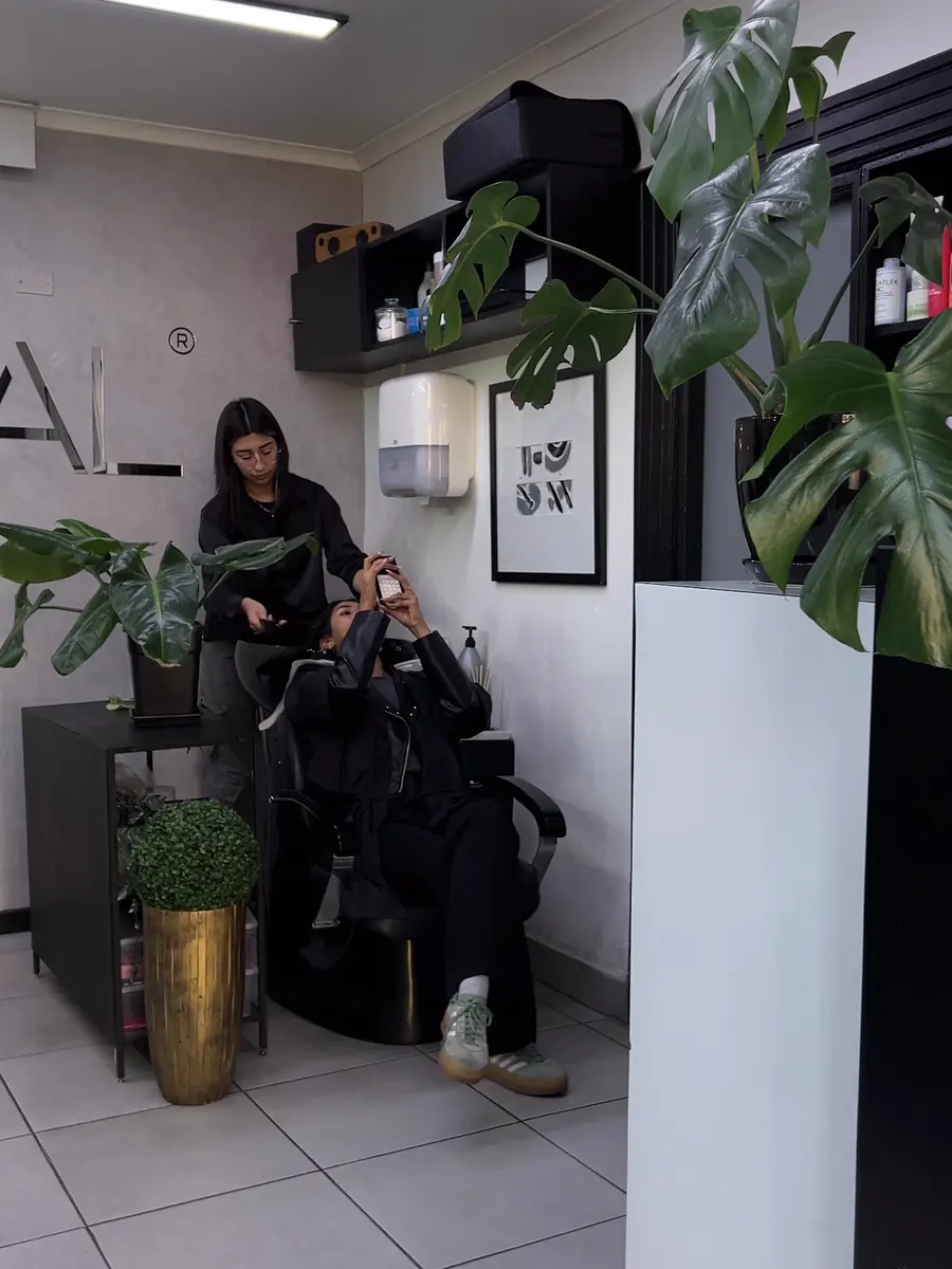 Salón del estudio con sillones negros, plantas y piso de cerámica blanca